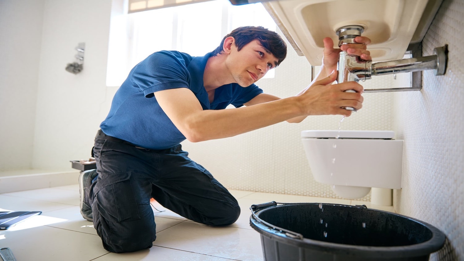 Plumber repairing the drain beneath a bathroom sink